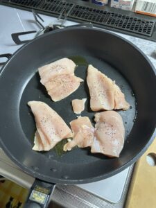 フライパンにオリーブオイルを入れて鶏むね肉を焼いている写真